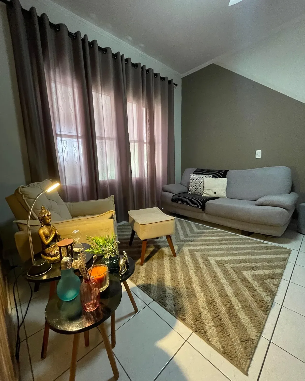 Sala de atendimento do consultório de psicologia da Sabrina Bordon em Campinas, com sofá cinza, poltrona, cortinas e tapete